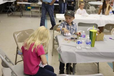 Two children sitting at a table with craft supplies, one girl and one boy.