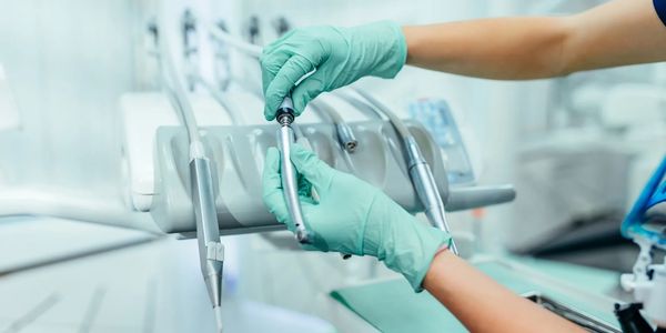Dentist wearing gloves handling dental instruments in a clinic.