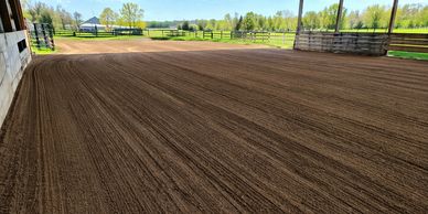 Freshly groomed dirt arena under a covered structure with a scenic background.