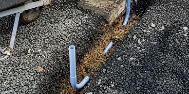 Trench with PVC pipes being installed in gravel ground.