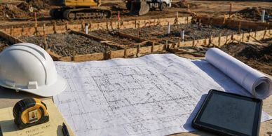 Construction site with blueprints, hard hat, and measuring tape on a table.