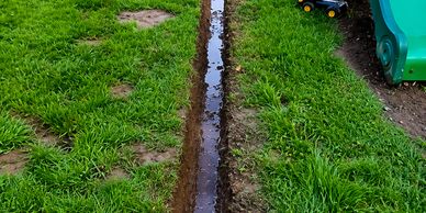 A narrow trench filled with water runs through a grassy yard.