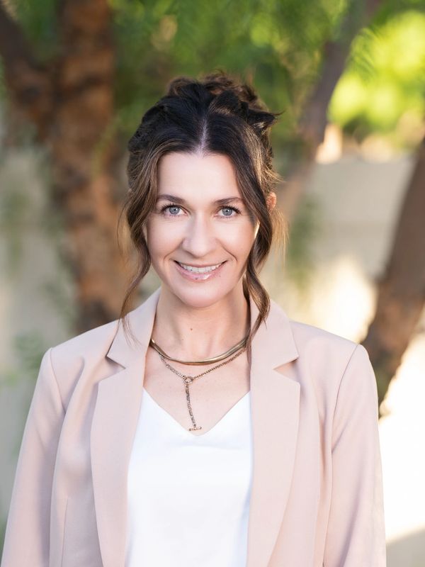A smiling woman in a beige blazer and white top outdoors.