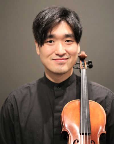 Young man holding a violin and smiling at the camera.