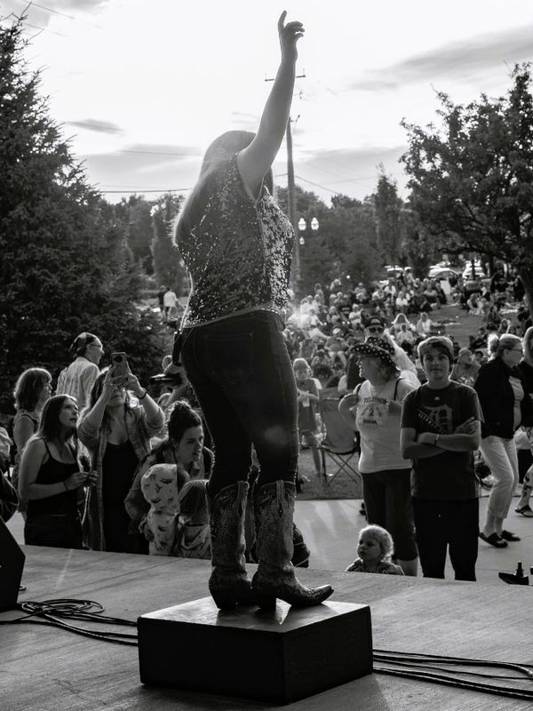 Performer on stage gestures to a crowd at an outdoor event.