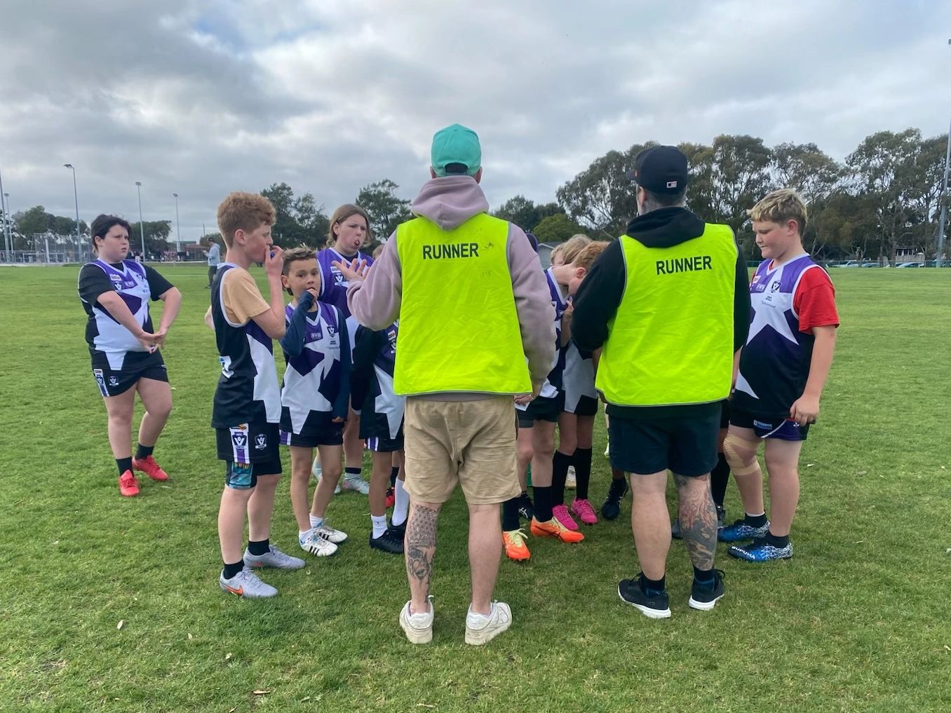 Youth sports team receiving coaching from two runners on a green field.