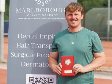 Man smiling and holding a red plaque in front of Marlborough Clinic Belfast banner.