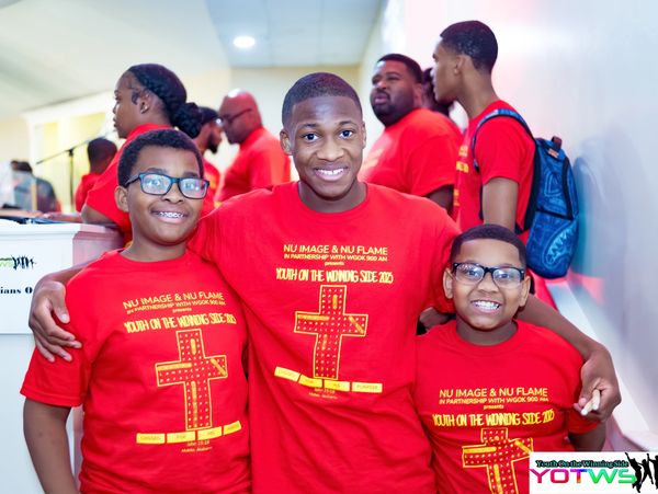 Three boys wearing matching red event T-shirts smiling at the camera indoors.