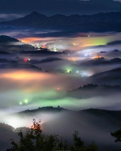 Misty night view of a valley with colorful lights.