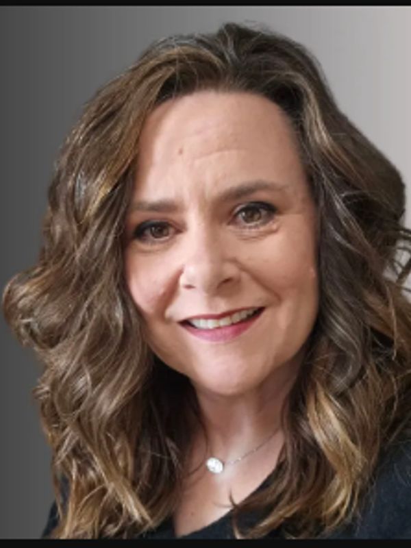 Smiling woman with wavy, highlighted hair and a necklace.