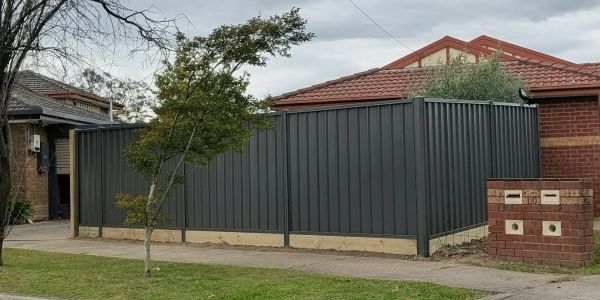 Gray metal fence enclosing a corner yard with a small tree and brick mailbox.
