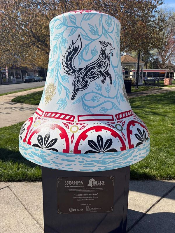 Decorative bell sculpture with a fox design in a park setting.