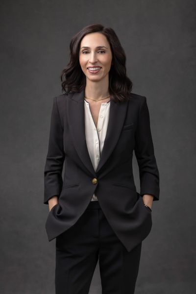 Professional woman in a black suit smiling confidently against a dark background.