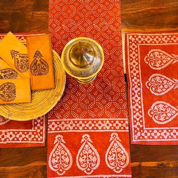 Orange table setting with patterned mats, leather wallets, and a brass container.
