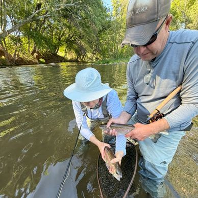 Two people holding freshly caught fish in a river.