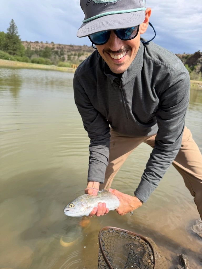 Smiling man releasing a fish into a lake during a sunny day.