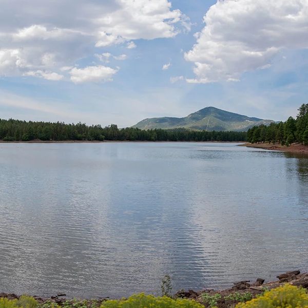 Serene lake with mountains and forest under a partly cloudy sky.