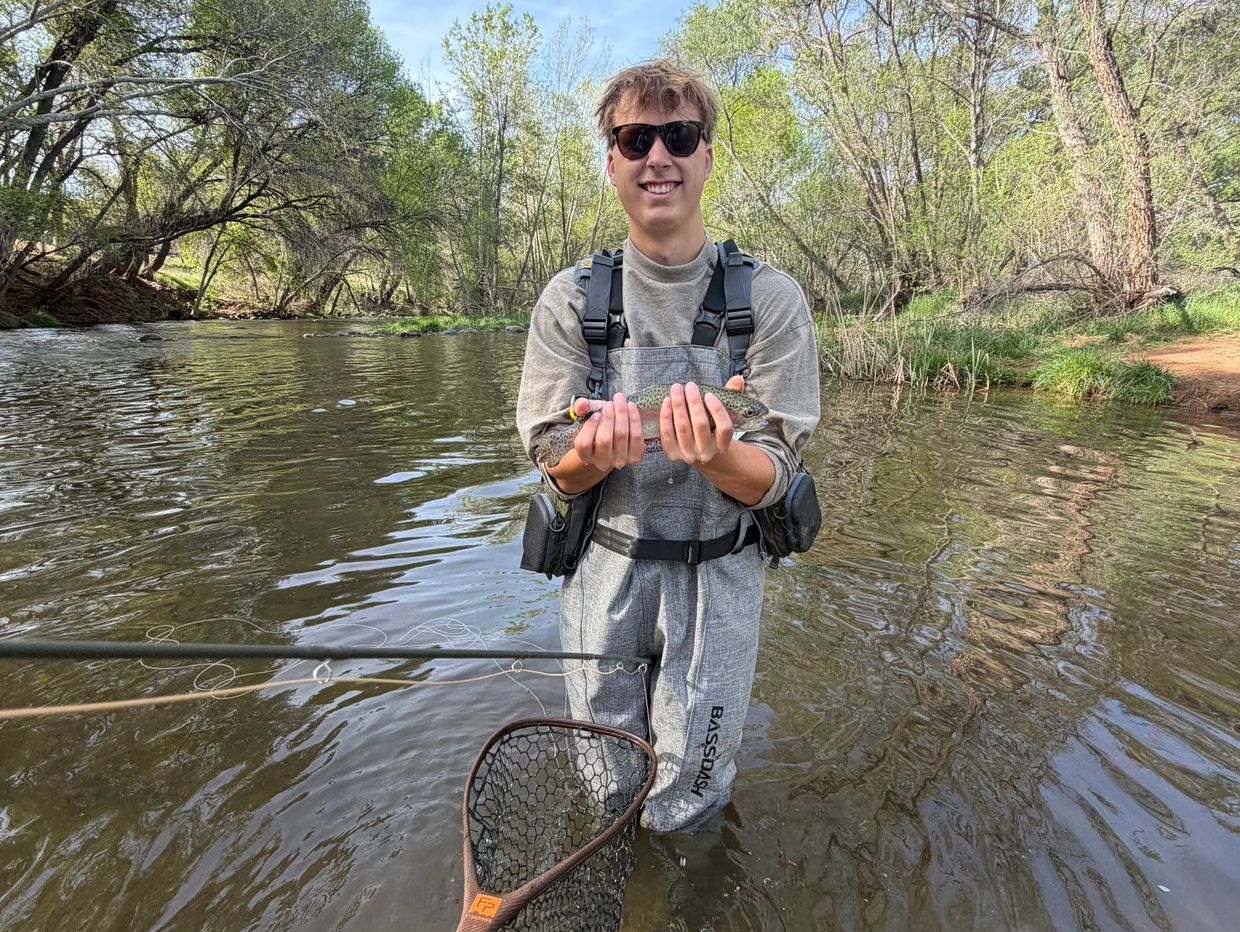 Young man holding a freshly caught fish in a river, smiling.