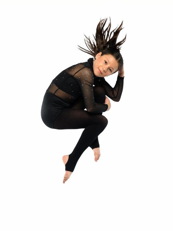 Young girl in black dance outfit mid-jump with hair flying.