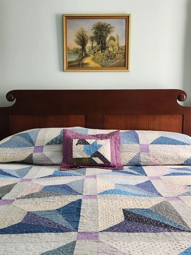 Our bed covered by one of Carol's handmade quilts, with a bucolic painting hanging overhead