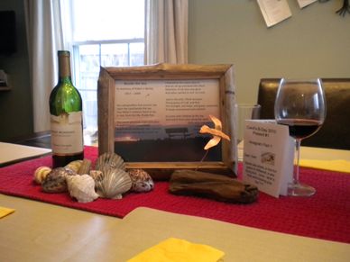 Still life of this poem in a driftwood frame, a wine bottle and glass, and seashore objects 