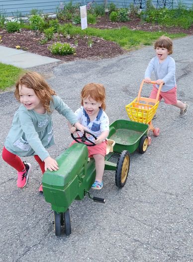 Three grandchildren playing on our driveway with toy tractor and trailer