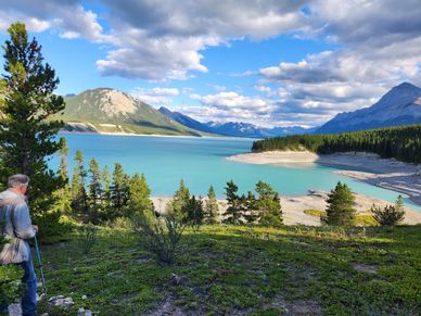 me standing at top of a hill with trekking poles, by a big blue mountain lake in the Canadian Rockie