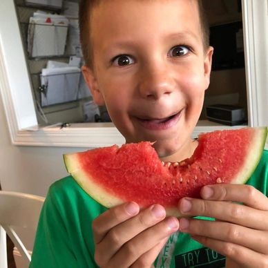 A smiling grandson eating watermelon which is missing a smile-shaped bite mark