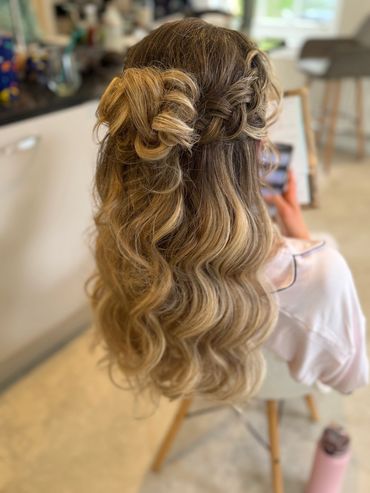 Elegant half-up hairstyle with loose curls and a braided detail.