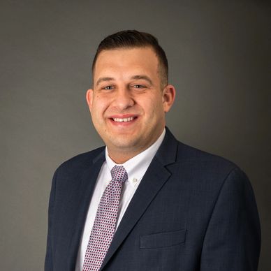 Professional man in suit smiling against a gray background.