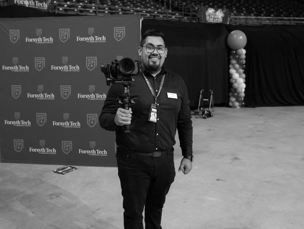 Videographer holding a camera on a gimbal in front of a step & repeat Commencement Graduation. 