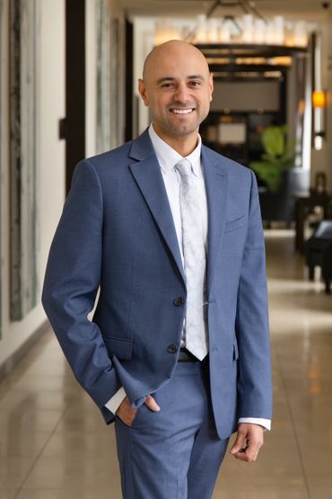 Smiling man in a blue suit standing confidently indoors.