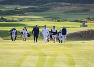Golfers walking on a golf course with caddies.