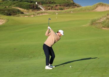 Golfer in mid-swing on a green golf course.