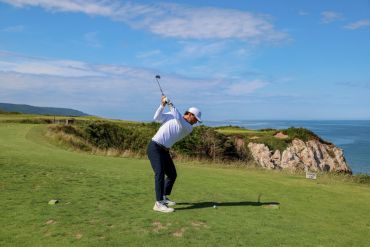 Golfer preparing to swing on a scenic coastal golf course.