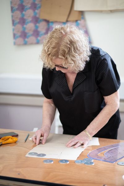 A woman works on a sewing pattern at a table with tools.