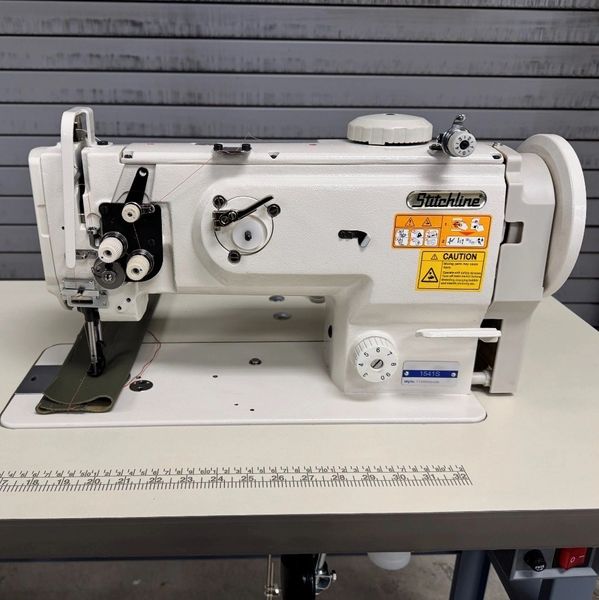 A white industrial Stitchline sewing machine on a table with a measuring ruler.