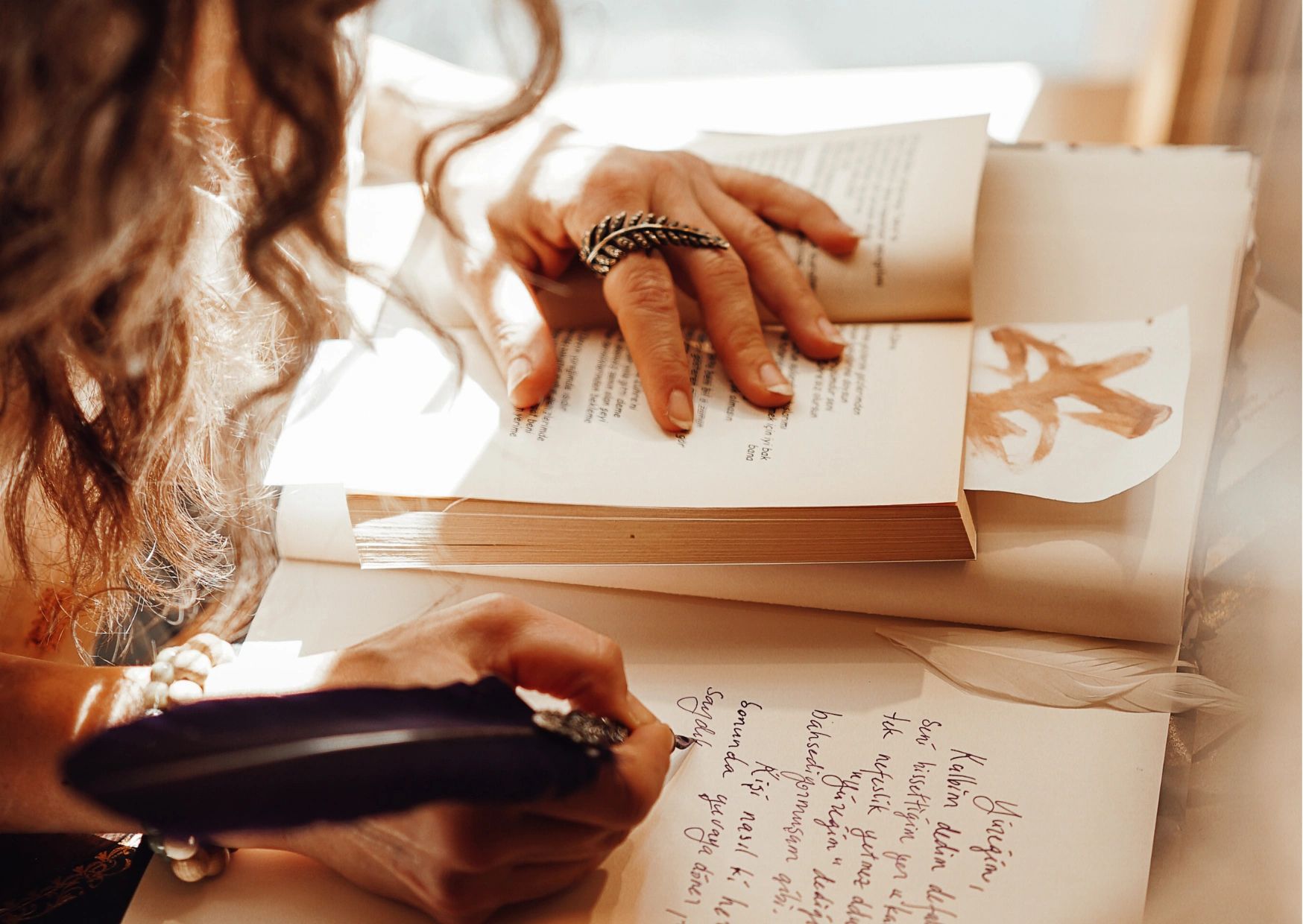 Person writing with a feather pen next to an open book.