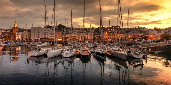 Sailboats docked at sunset in a harbor with city buildings.