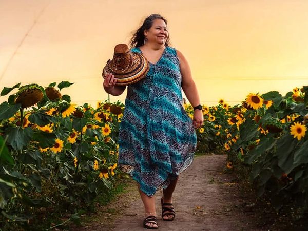 Woman in a blue dress walking through a sunflower field at sunset.