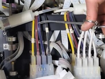 Close-up of a hand adjusting ink tubes in a printer.