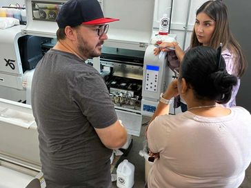 Three people discussing a machine in a workshop.