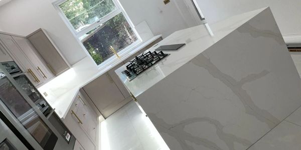 Modern kitchen with marble island and built-in stove under natural light.