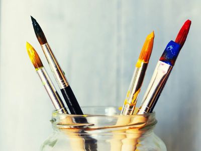 Paintbrushes with colorful paint in a glass jar.