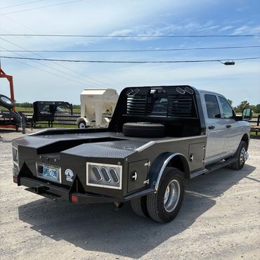Silver pickup truck with a custom flatbed in a rural area.