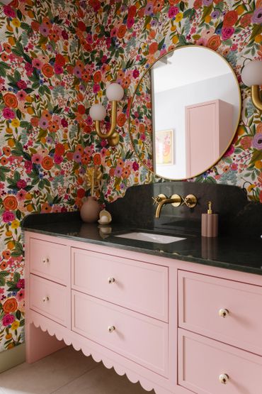 Pink vanity with floral wallpaper and gold accents in a bathroom.