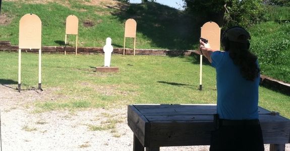 Person aiming a handgun at targets on a shooting range outdoors.