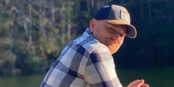 Man in a plaid shirt and cap outdoors.