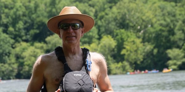 Man wearing a hat and sunglasses by the water.