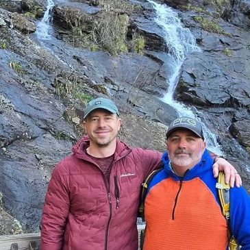 Two men posing near a rocky waterfall.
